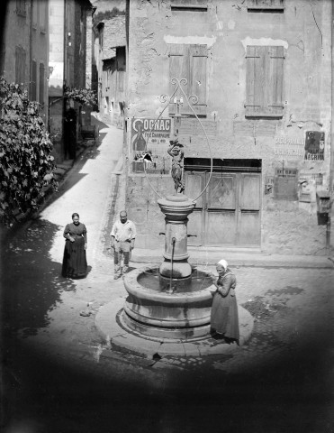 Buis-les-Baronnies.- La Place aux Herbes et la fontaine, rue du Puits communal. Romain Layraud, menuisier, la femme au bonnet est Madame Thibaud, cafetière.