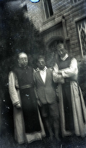 Deux hommes en habit religieux et un jeune garçon posant debout devant un bâtiment.